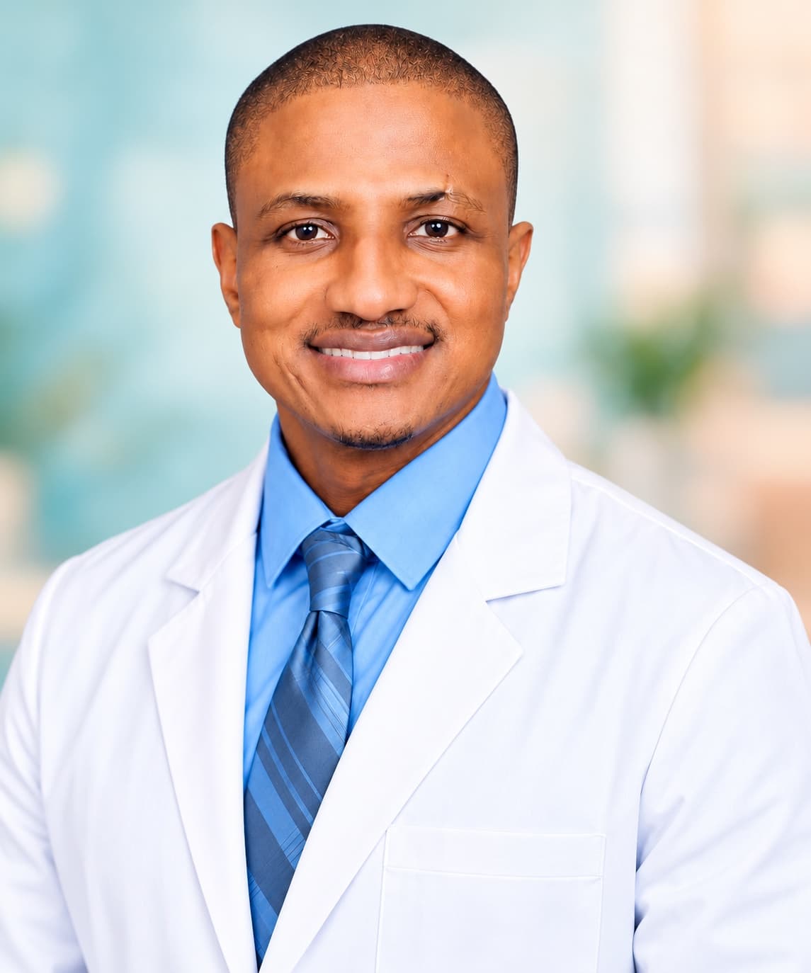 Olalekan “Kenny” Adefowokan smiling, wearing a white coat, blue shirt and tie